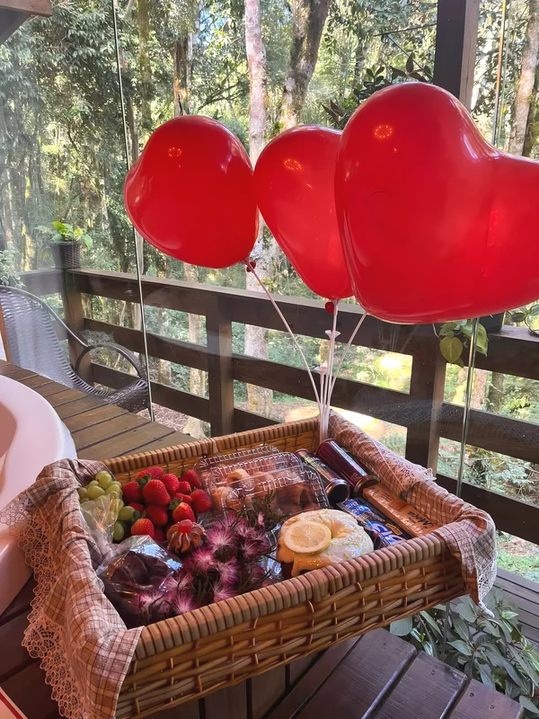 Cesta de café da manhã de aniversário com balões de coração na varanda, de frente para a mata