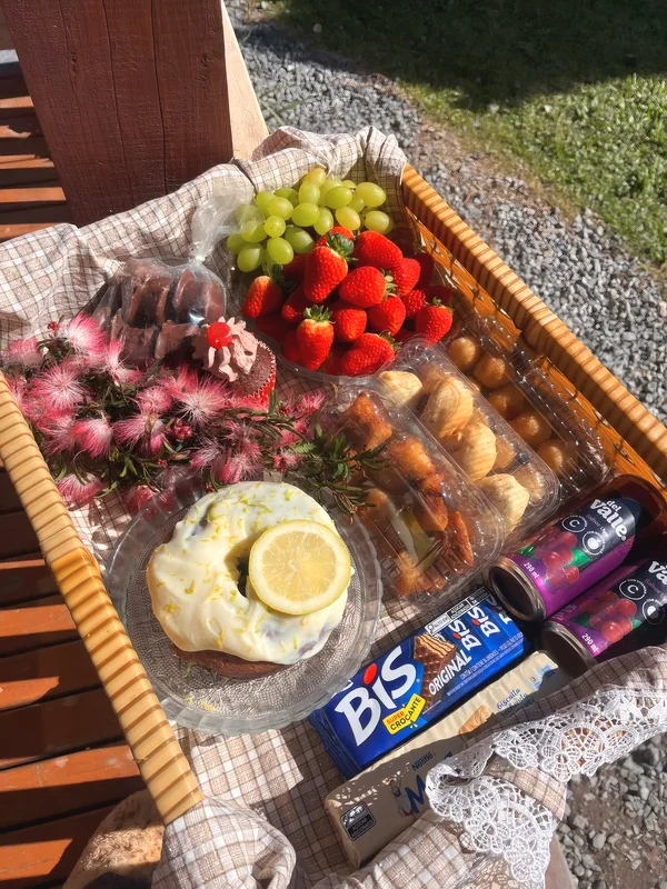 Cesta de aniversário com bolo de limão, cupcake, morangos, uvas, salgadinhos, chocolate, sucos e flores