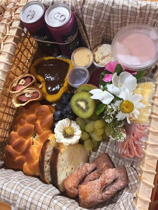 Cesta do café colonial vista de cima, com pão trançado, cuca, frutas, frios, iogurte e flores