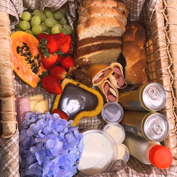 Cesta do café colonial com mamão, morangos, uvas, pães, bolo, enroladinhos e sucos