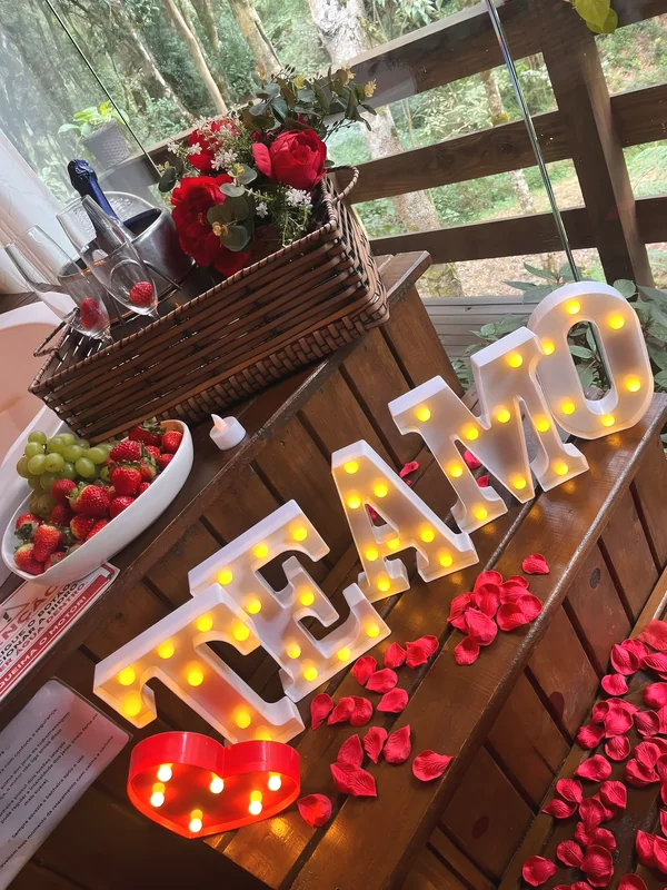 Letreiro Te amo iluminado com coração, pétalas, frutas e espumante