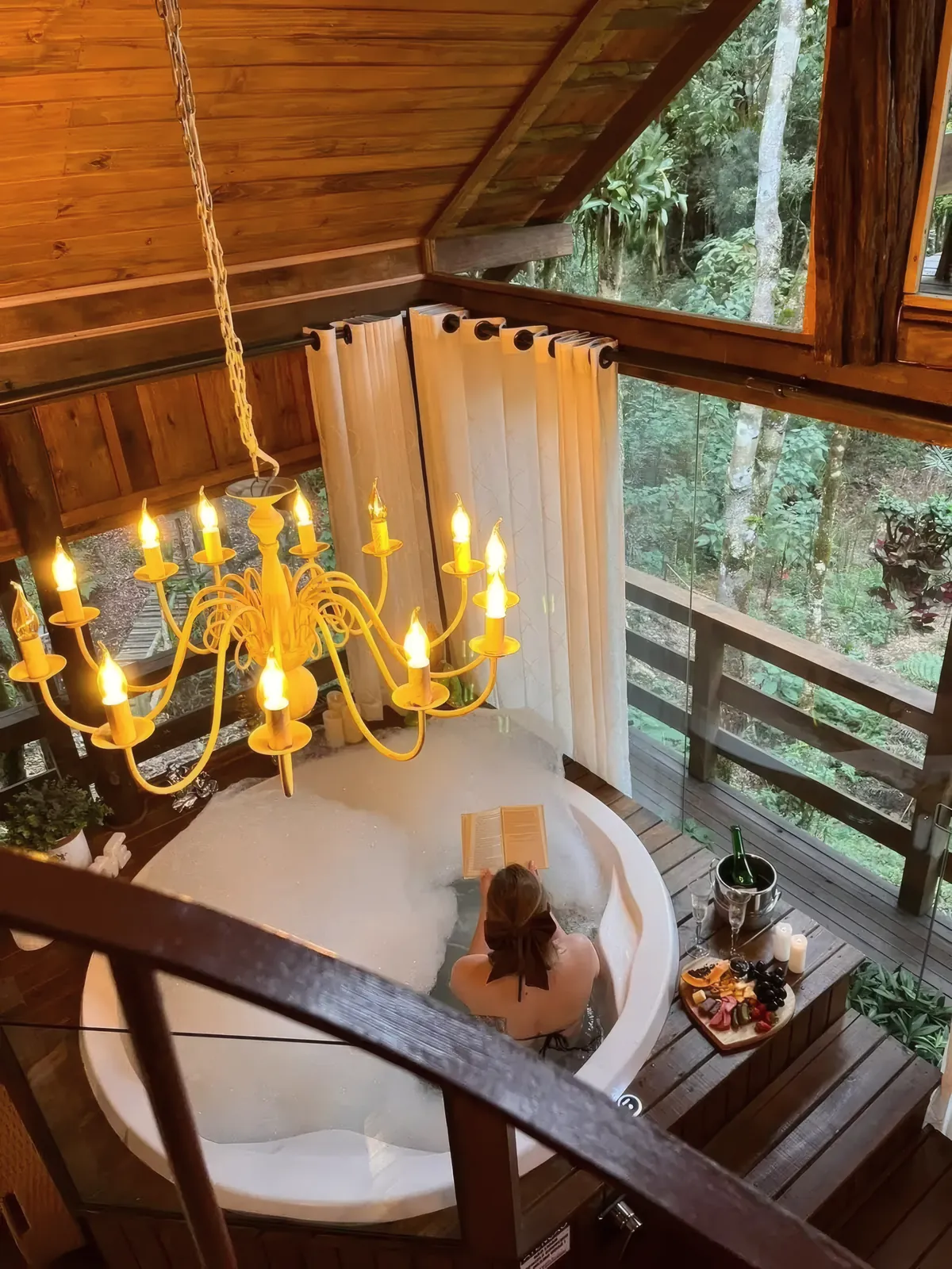 Hidromassagem redonda com lustre de velas, na varanda envidraçada da mata